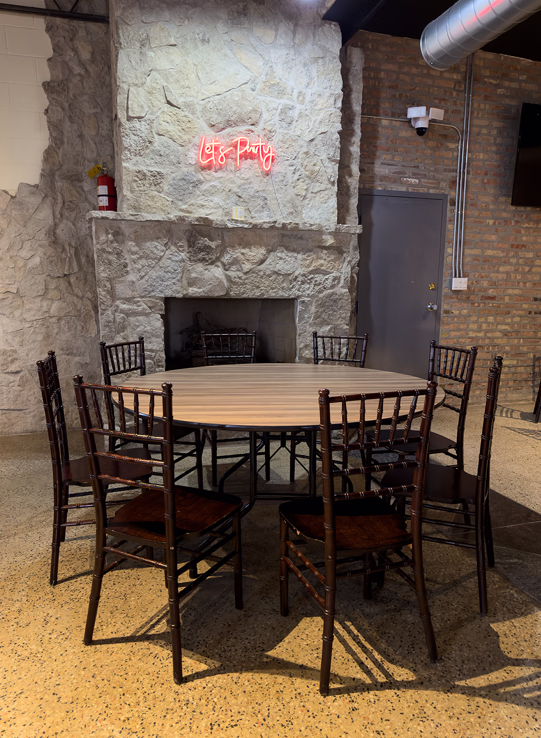 Private event dining space at El Cubanito in Chicago featuring a round banquet table, Chiavari chairs, stone fireplace, and neon party sign